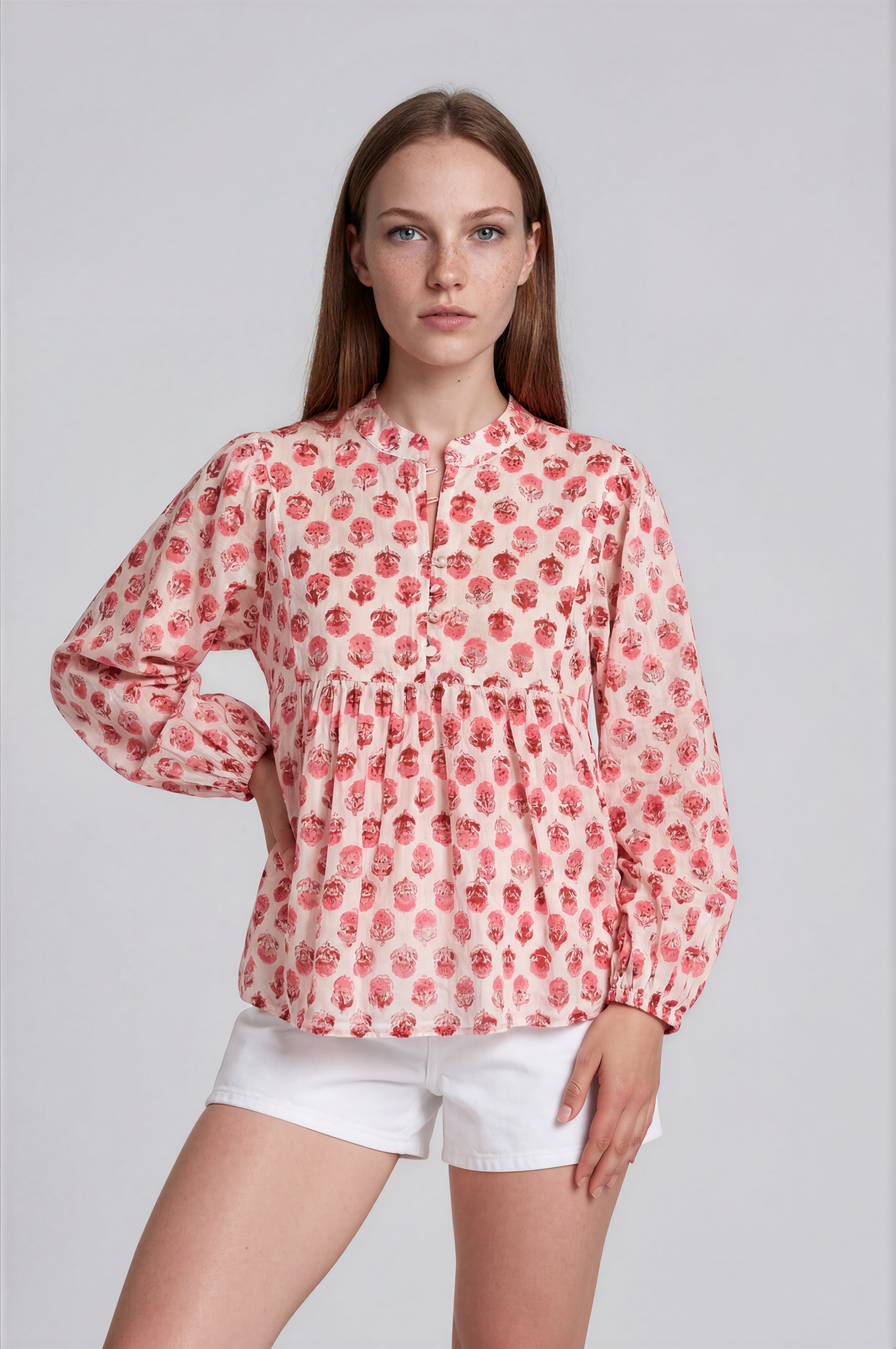 Woman wearing a red floral blouse and white shorts on a light gray background