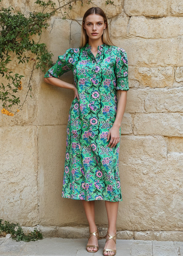 Woman wearing a green floral dress standing against a stone wall.
