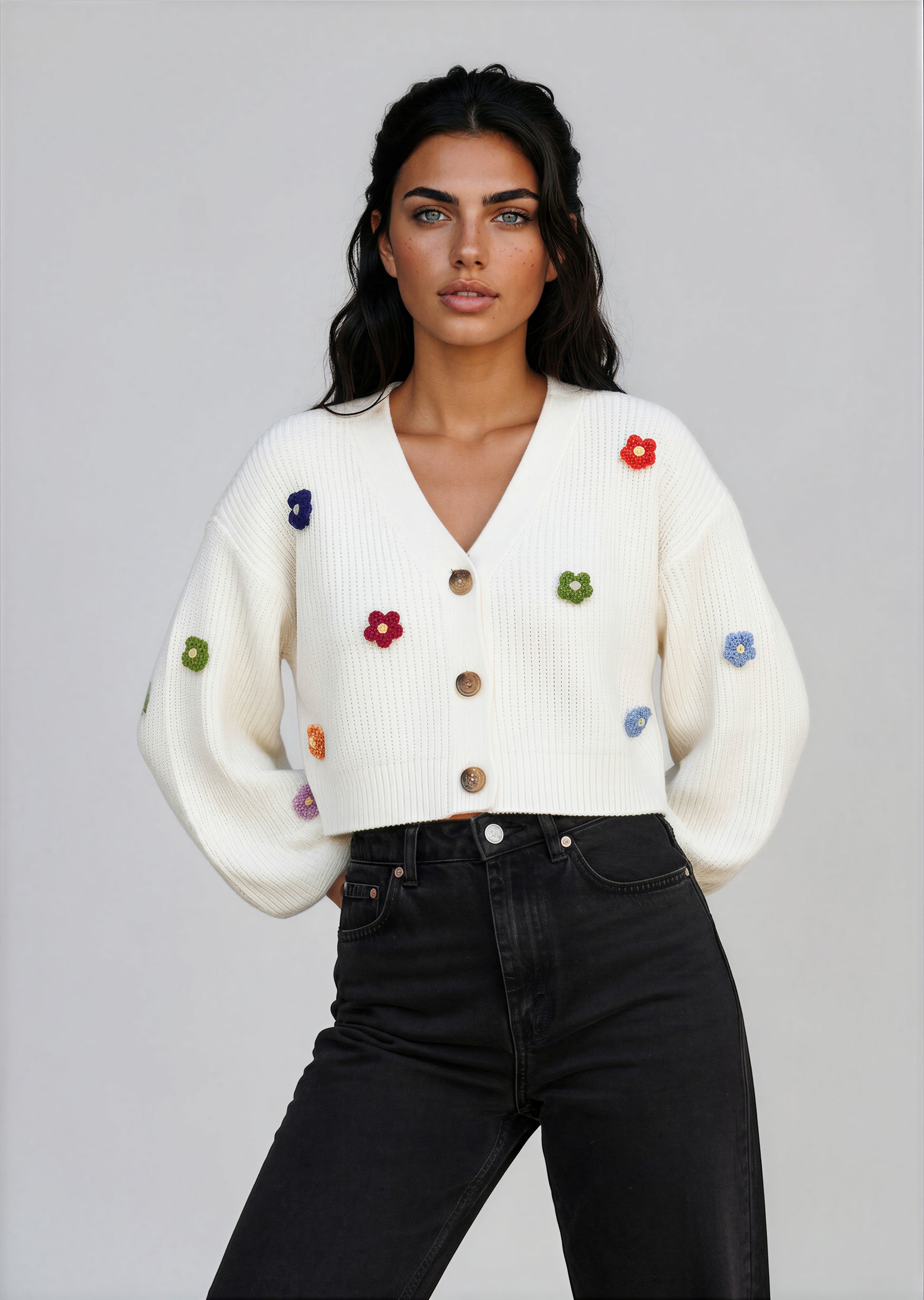 Woman wearing a white sweater with colorful buttons against a stone wall with greenery.