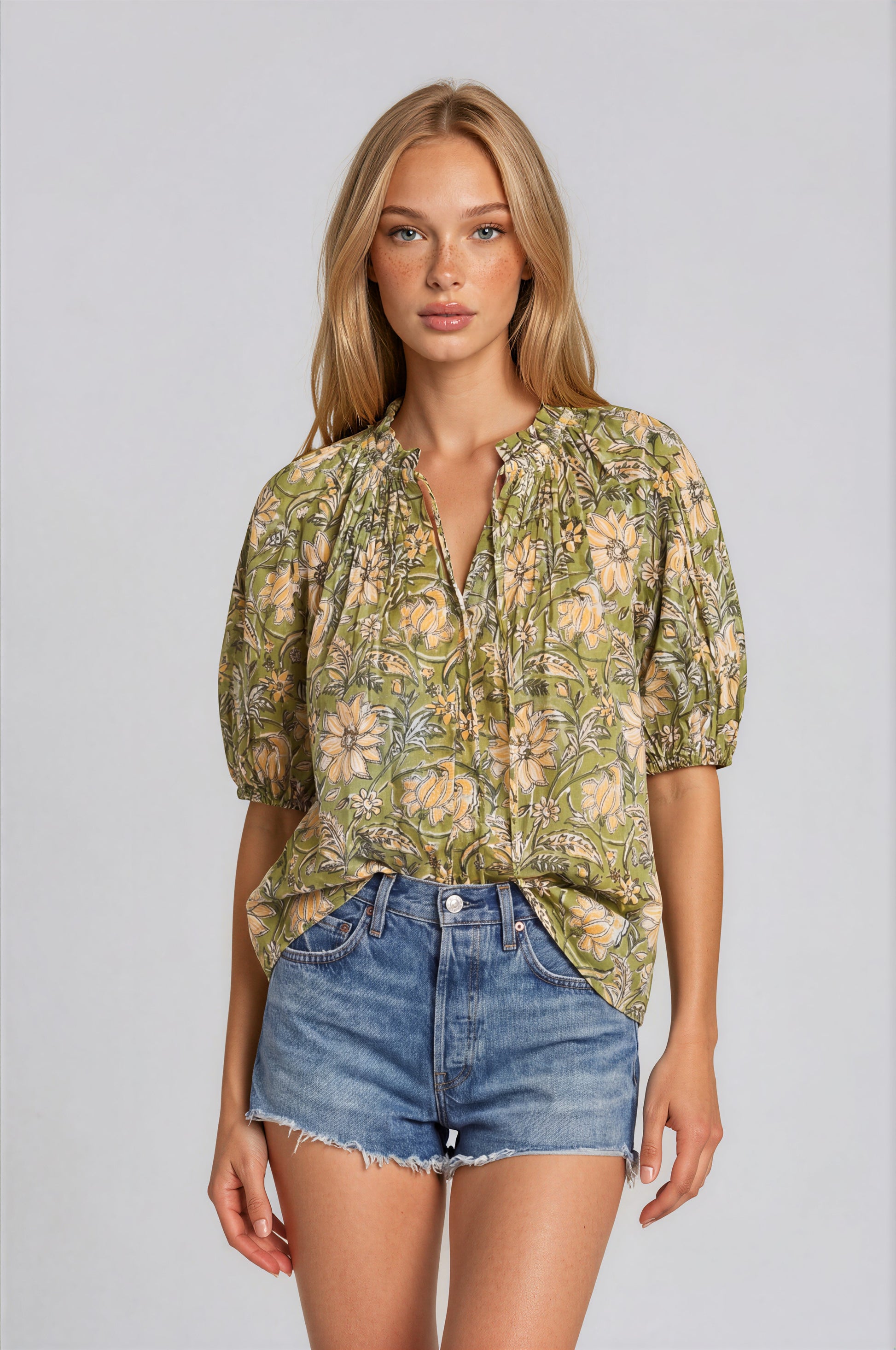 Woman wearing a floral blouse and denim shorts on a plain background