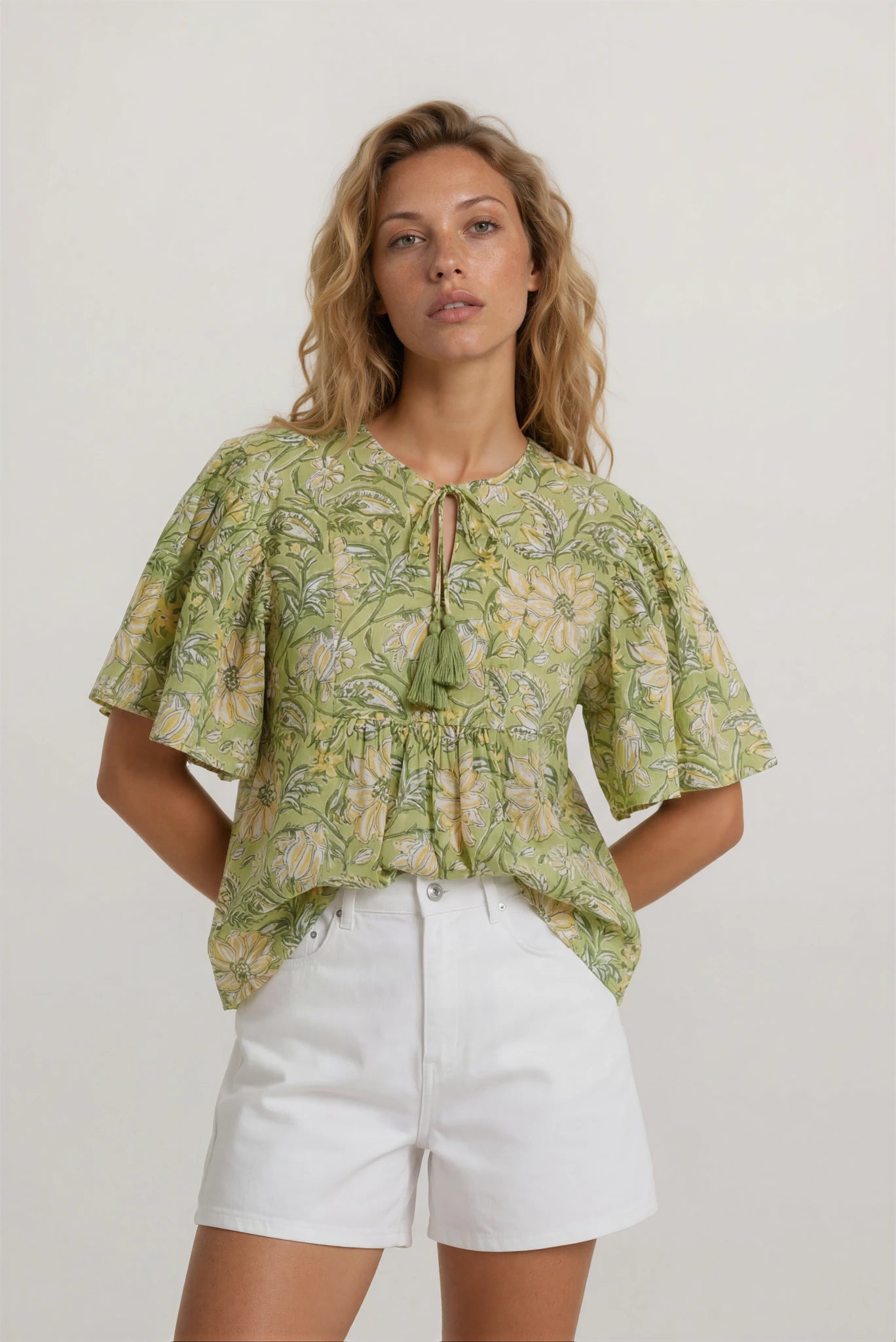 Woman wearing a green floral blouse and white shorts on a plain background