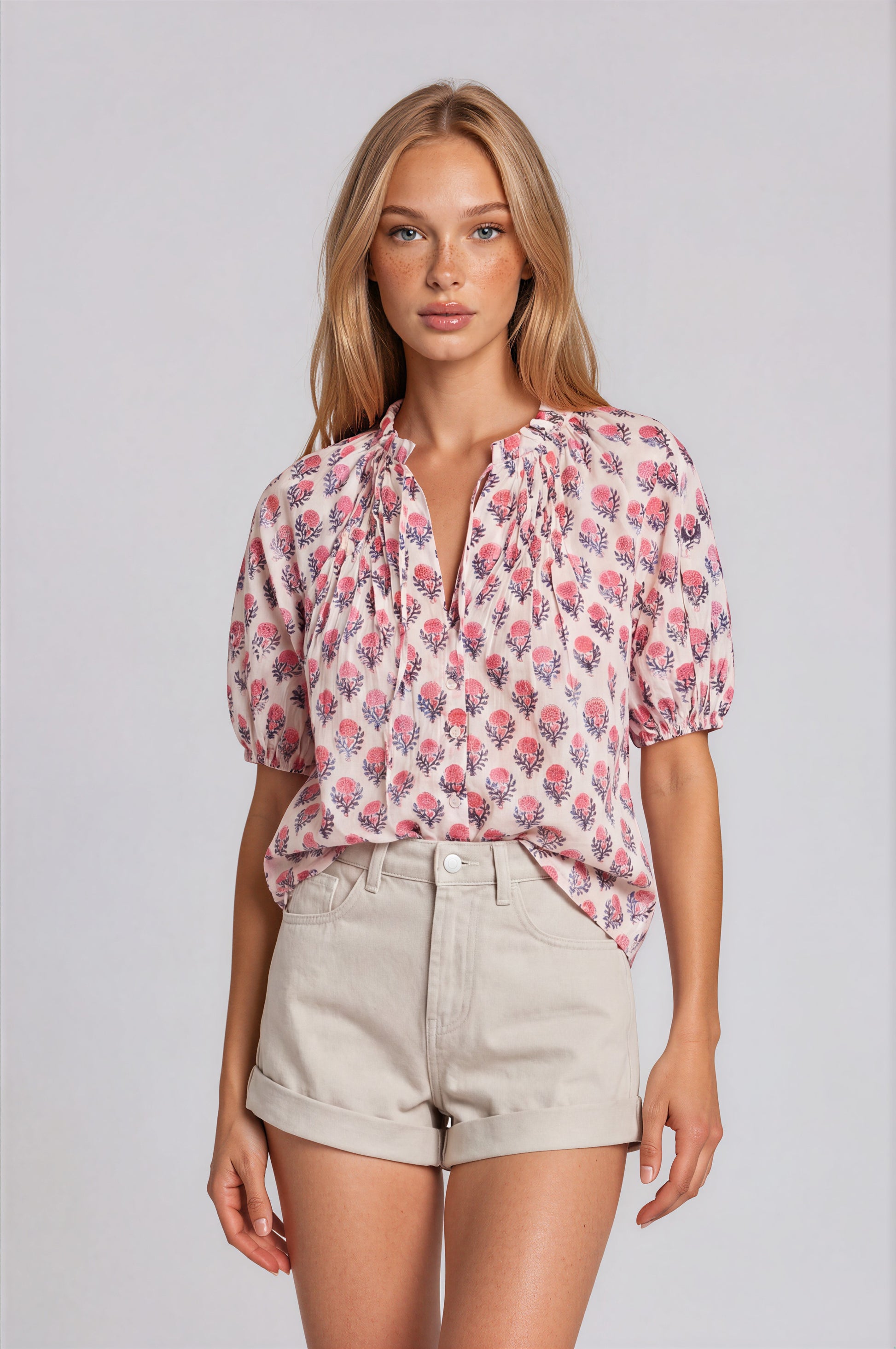 Woman wearing a floral blouse and beige shorts on a plain background
