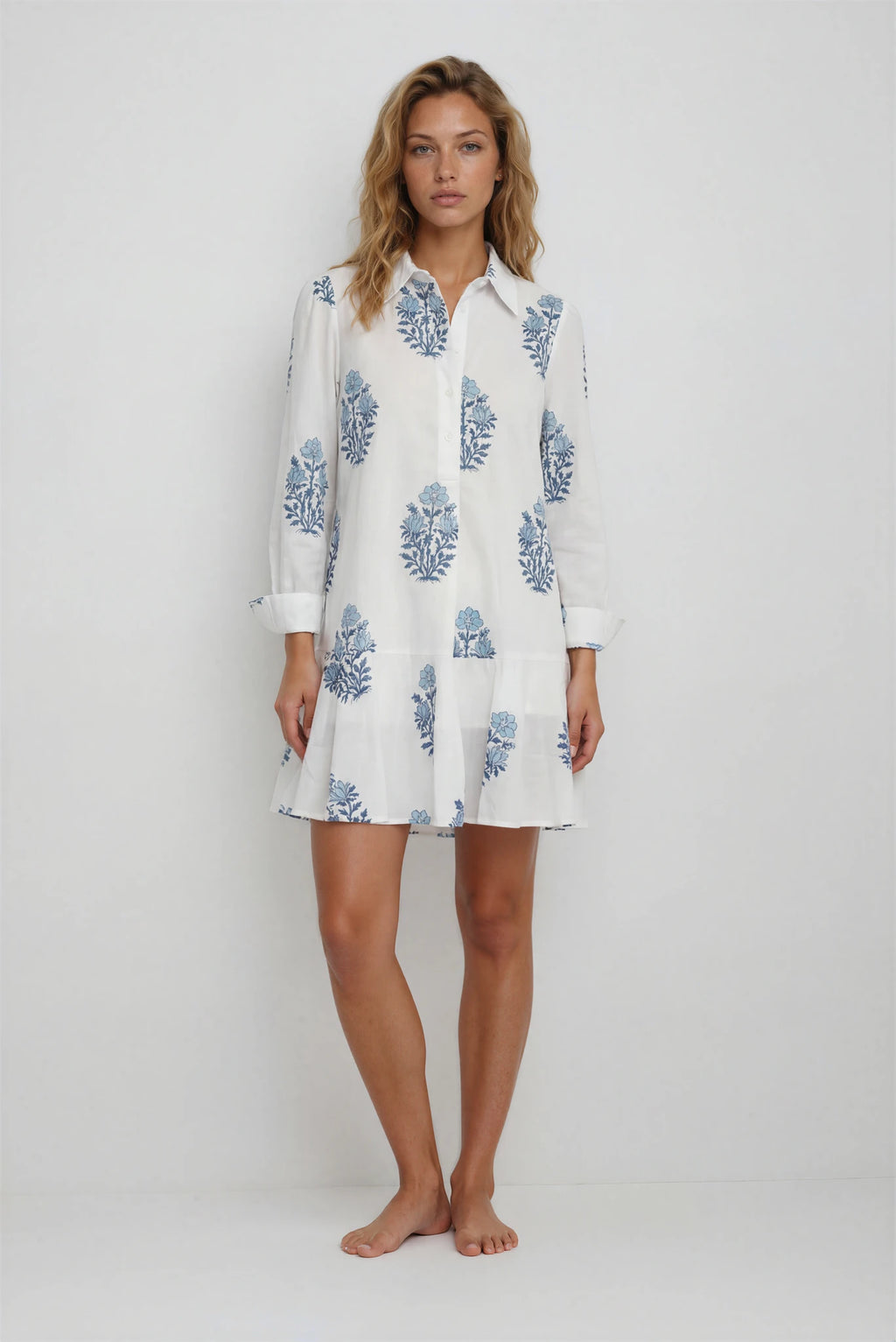 Woman wearing a white dress with blue floral patterns on a plain background