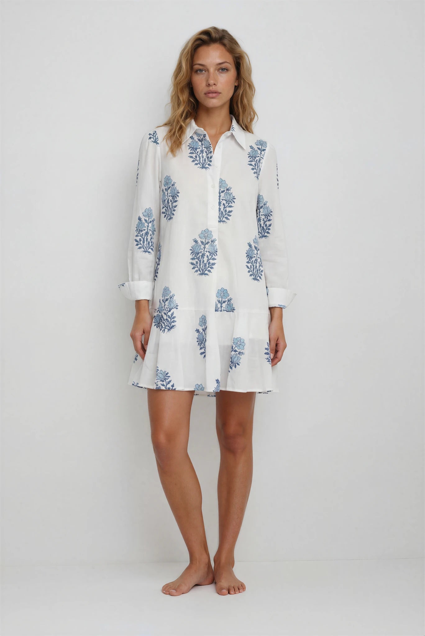 Woman wearing a white dress with blue floral patterns on a plain background