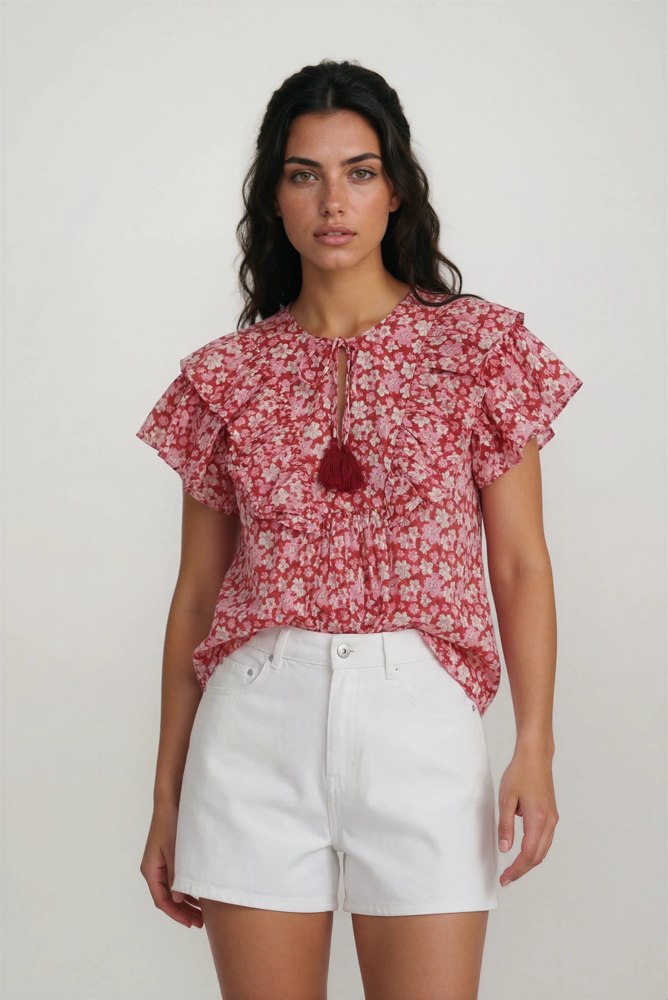 Woman wearing a red floral blouse and white shorts on a plain background