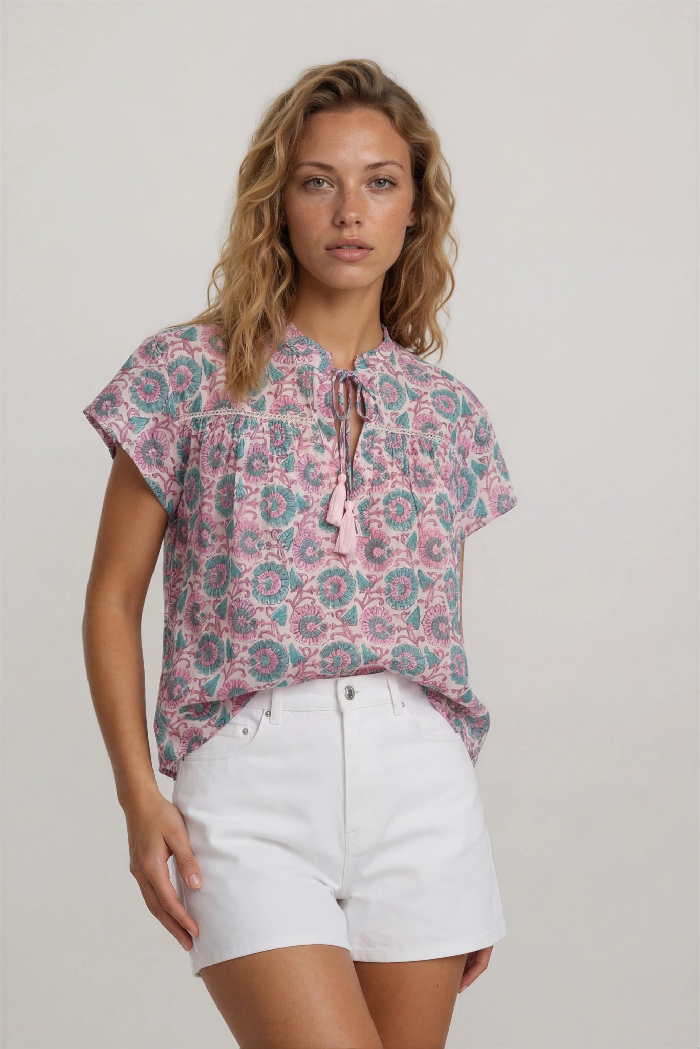 Woman wearing a floral blouse and white shorts on a plain background